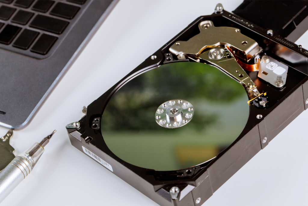 An open hard drive beside a laptop on a white surface