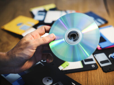 A person holding a CD ROM with a lot of floppy disks in the background