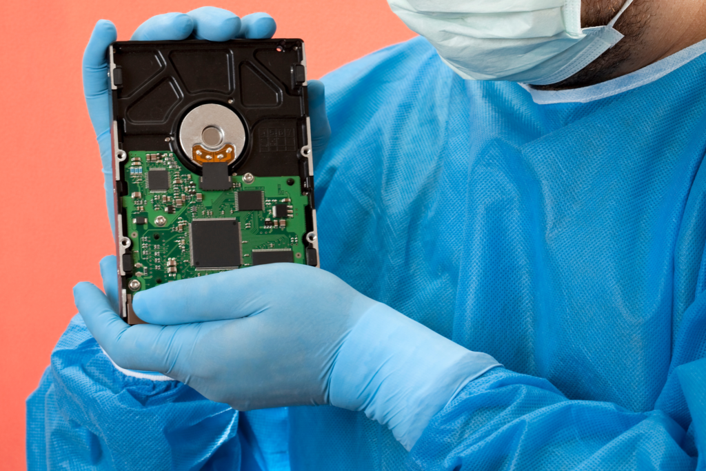 A technician with rubber gloves and surgical mask and gown holding up a hard drive with newly-recovered data